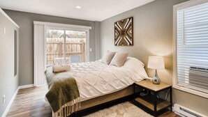 A bedroom with a bed, bedside table, lamp, and a window with blinds.