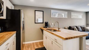 A compact kitchen with a black refrigerator, wooden countertop, and a sink. There are cabinets, a coffee maker, and a framed picture on the wall.