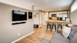 A modern living room with a flat-screen TV, a sofa, and a coffee bar with stools.