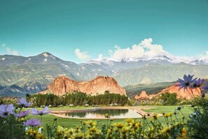 A golf course with a pond, mountains, and flowers in the foreground.