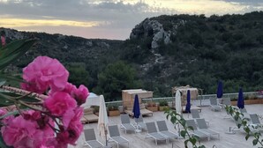 Zona de piscina con sillones reclinables y sombrillas, con vistas a un paisaje montañoso.