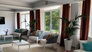 Un salón amplio con un ventanal grande, sofás blancos y varias macetas con plantas.