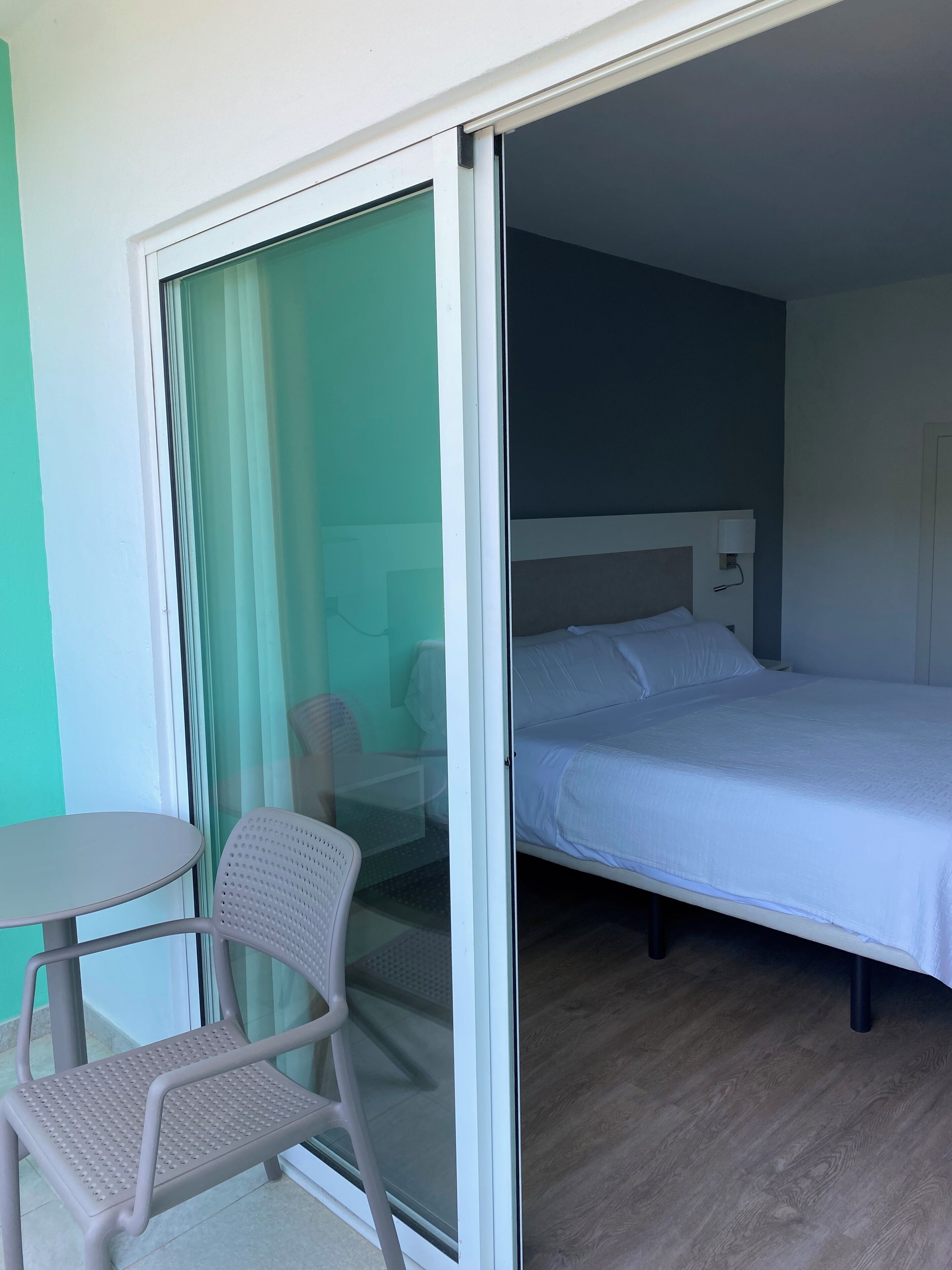 Een hotelkamer met een bed, een stoel, een tafel en een glazen schuifdeur.