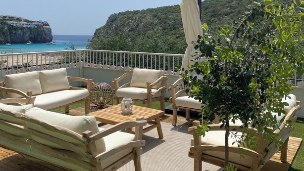 Una terraza de madera con mobiliario exterior, una planta en maceta y vistas al mar y acantilados.
