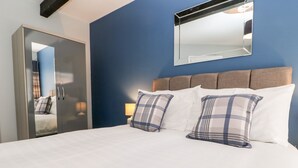 A hotel room with a bed, two pillows, a nightstand, a lamp, a mirror, and a wardrobe. - 3 Kings Mews (Richmond)