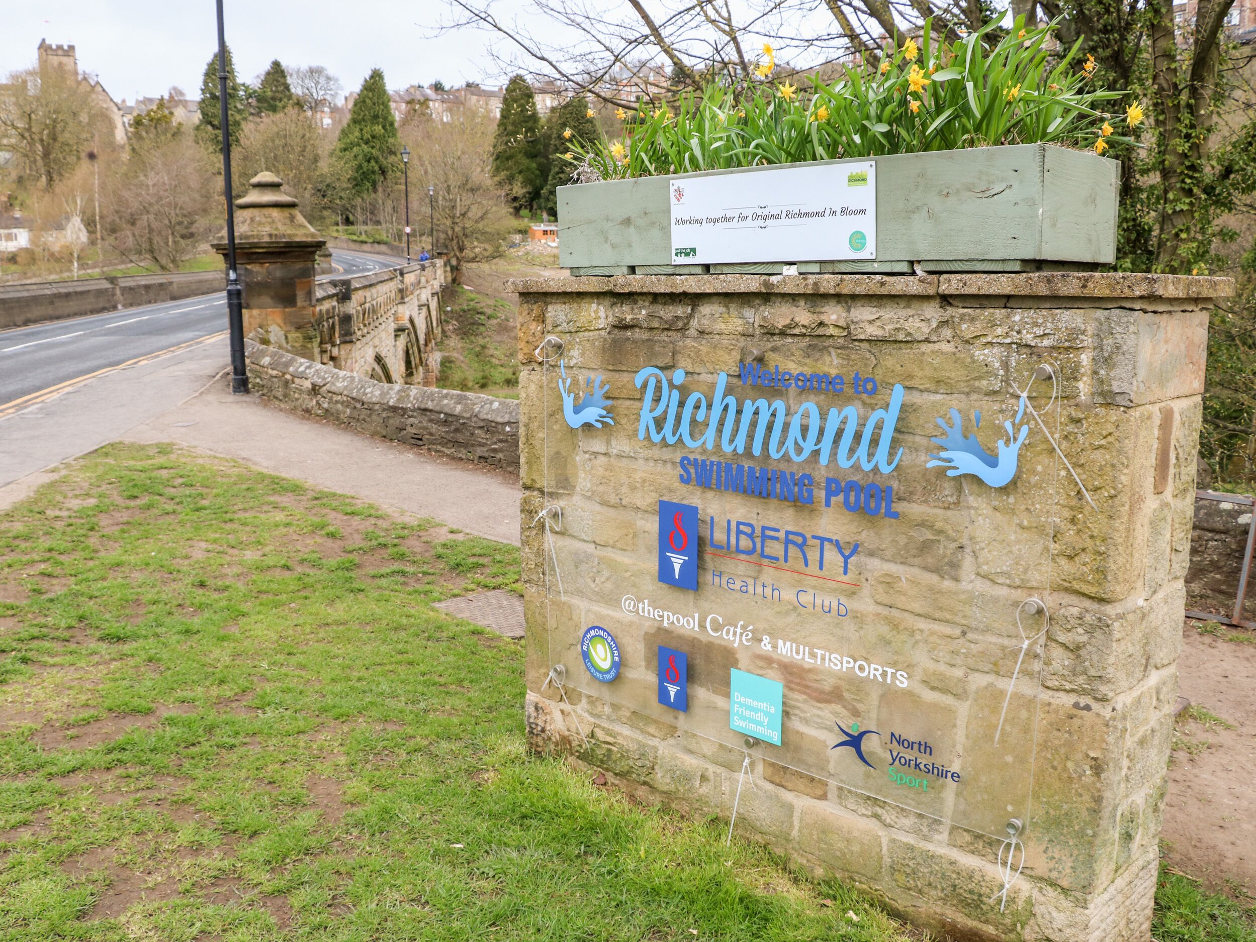 Un letrero de piedra con el texto 'Bienvenidos a la Piscina Richmond' y logotipos de Liberty Health Club, North Yorkshire Sport y Piscina Abarrotable para Personas con Demencia.