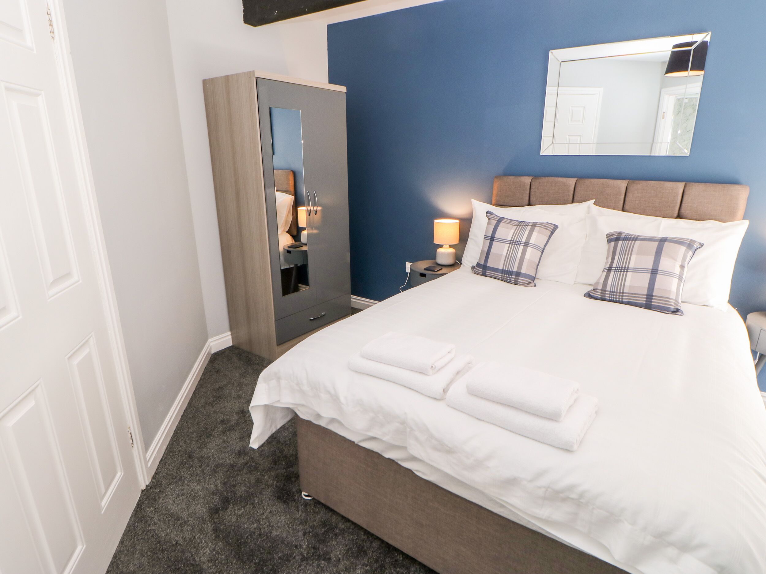 Quarto de hotel com cama, guarda-roupa, mesa de cabeceira com abajur e espelho na parede.