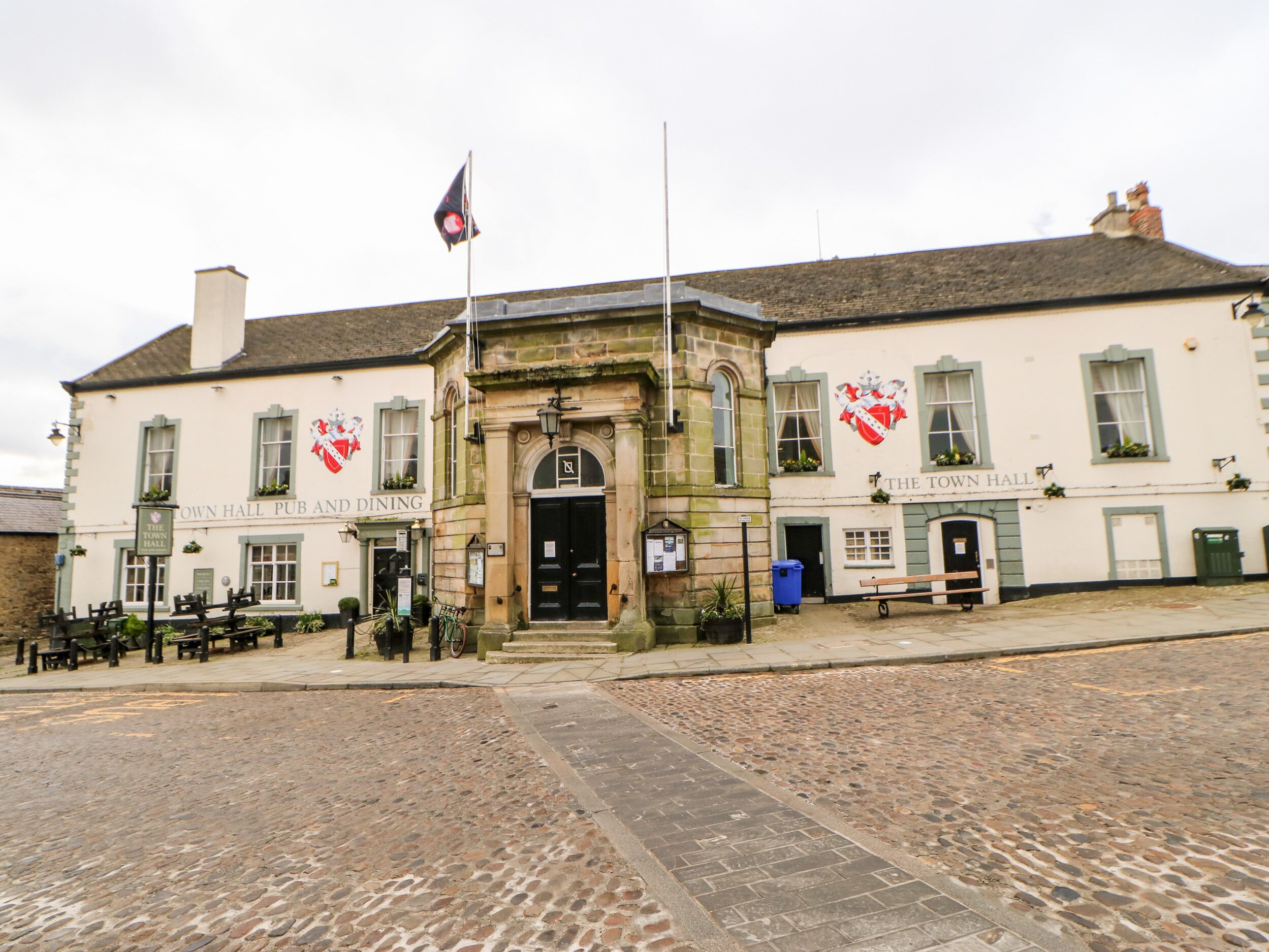 Un pub histórico y restaurante con un patio adoquinado, arquitectura tradicional y mesas al aire libre.