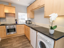 A modern kitchen with wooden cabinets, a stainless steel stove, a dishwasher, and a washing machine.