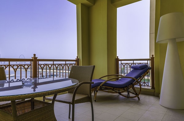 A balcony with wicker furniture, a glass table, and a view of the sea.