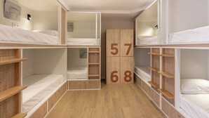 Une chambre de dortoir avec des lits superposés, des étagères en bois et un tableau d’affichage numérique.