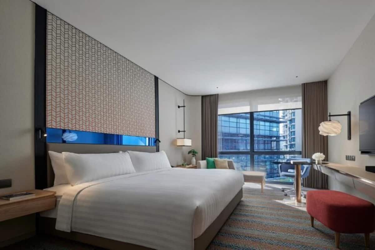 A hotel room with a large bed, a TV, a desk, and a view of the city.
