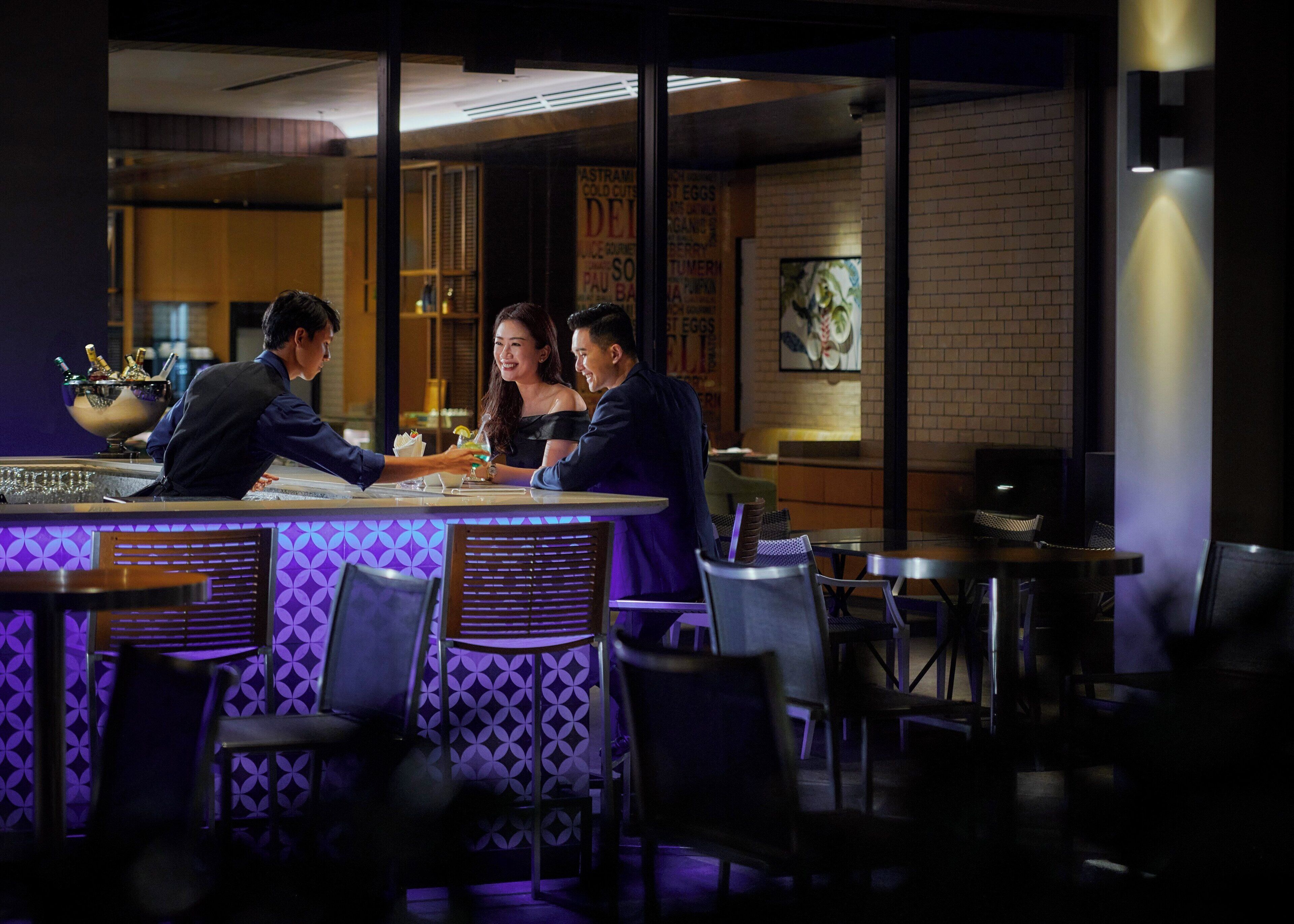 A dimly lit restaurant with a bar area, tables, and chairs.