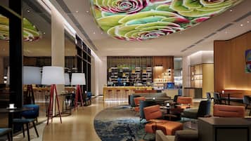Un moderno vestíbulo de hotel con área de bar, arreglos de asientos y un gran mural en el techo.