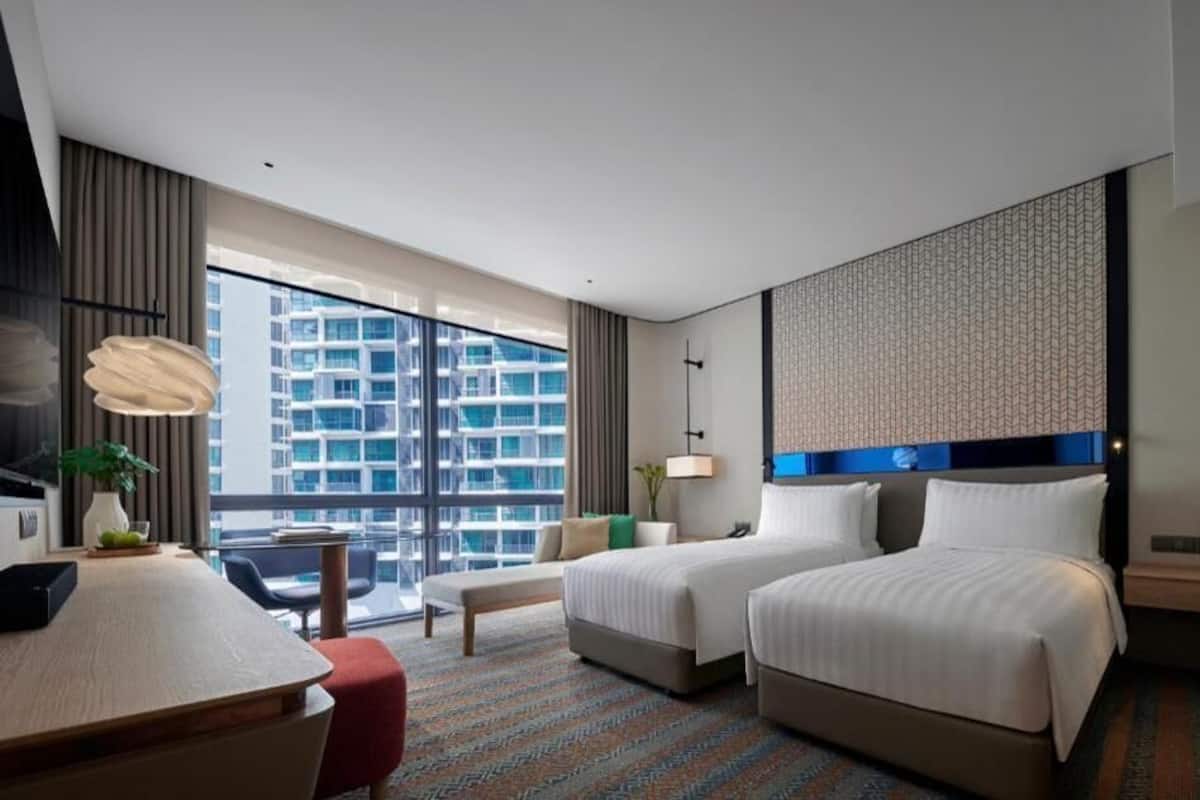 A hotel room with two beds, a desk, a chair, a large window with a city view, and a patterned wall.