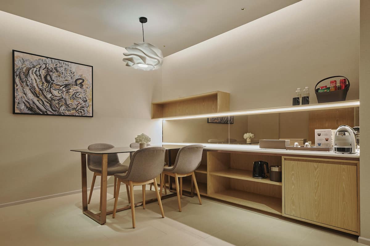 A modern kitchen with a dining area, featuring a wooden cabinet, a coffee machine, and a hanging light fixture.