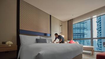 Quarto de hotel com cama grande, mesa de cabeceira com um vaso de flores, cabeceira moderna e vista de arranha-céus através de amplas janelas.