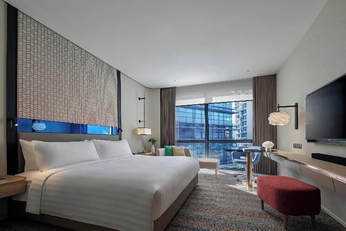 A hotel room with a large bed, a TV, a desk, and a view of the city.