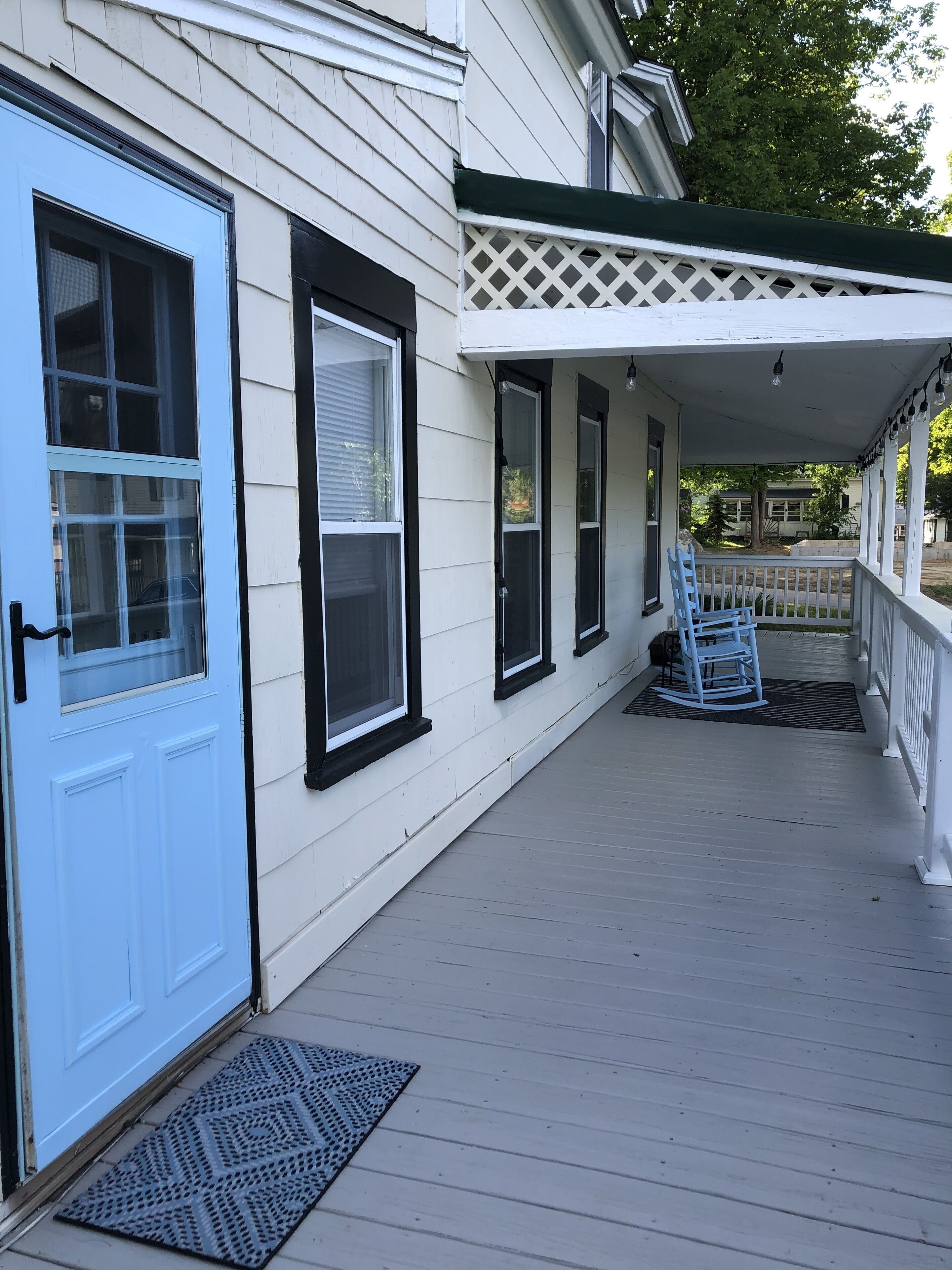 A porch with a blue door, white siding, and a covered area with a rocking chair.