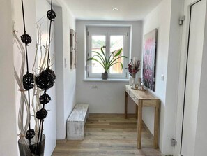 A hallway with a wooden bench, a table with decorative items, a potted plant by a window, and wall-mounted artwork. - StylishHomes NEST - A Cosy Adventure (Frauental an der Lassnitz)