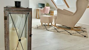 Una stanza in stile loft con soffitto alto, travi a vista in legno, un'ampia finestra a lucernario, una sedia moderna, un tavolino e una vetrina decorativa.
