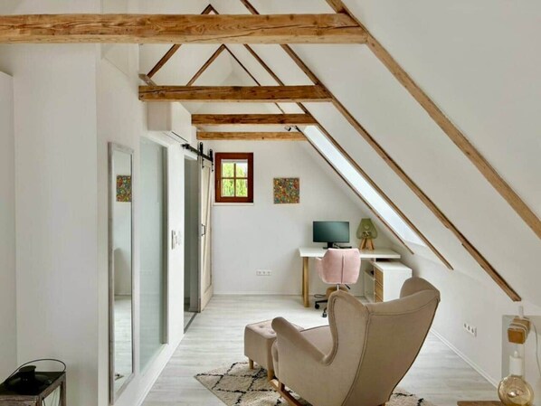 A room with a sloped ceiling, a desk with a computer, a chair, and a window.