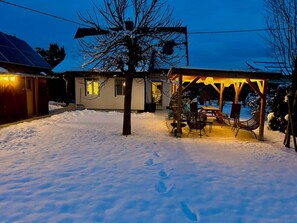 A snow-covered yard with a house, a covered patio with chairs, and a tree. - StylishHomes NEST - A Cosy Adventure (Frauental an der Lassnitz)