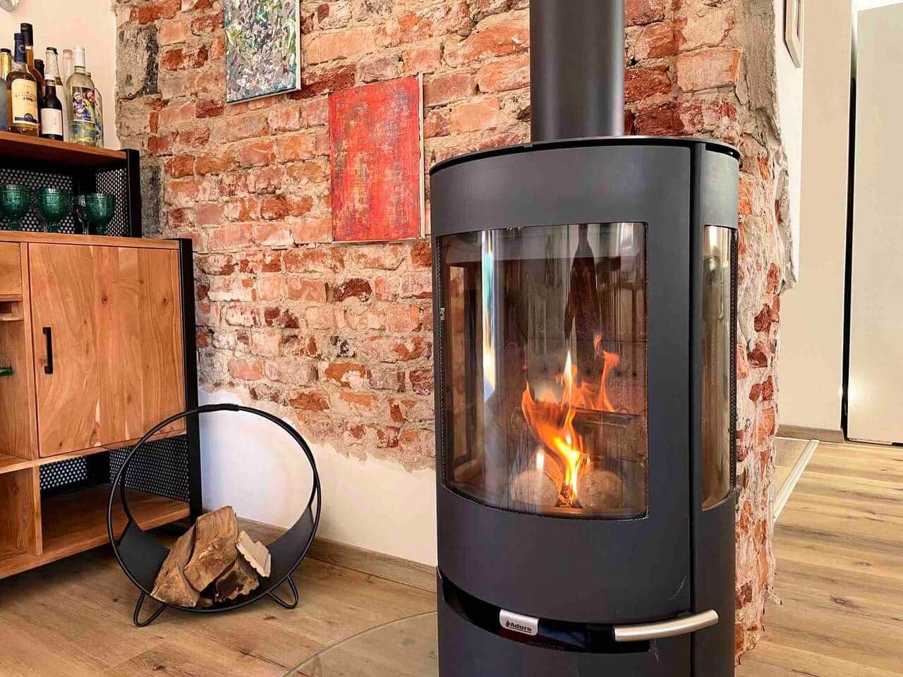 A wood-burning stove with a glass front, a wooden cabinet, and a brick wall.