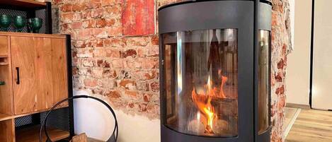 A wood-burning stove with a glass front, a wooden cabinet, and a brick wall.
