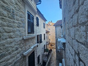 A narrow stone alleyway between buildings with shutters, a small balcony, and a tiled roof visible in the distance. - Athos Guesthouse (Kotor)