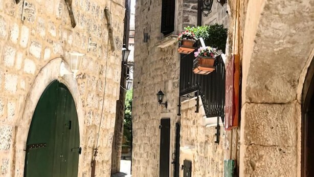 A narrow street with stone buildings, a green door, and a hanging sign for ATHOS STREET FOOD. - Athos Guesthouse (Kotor)