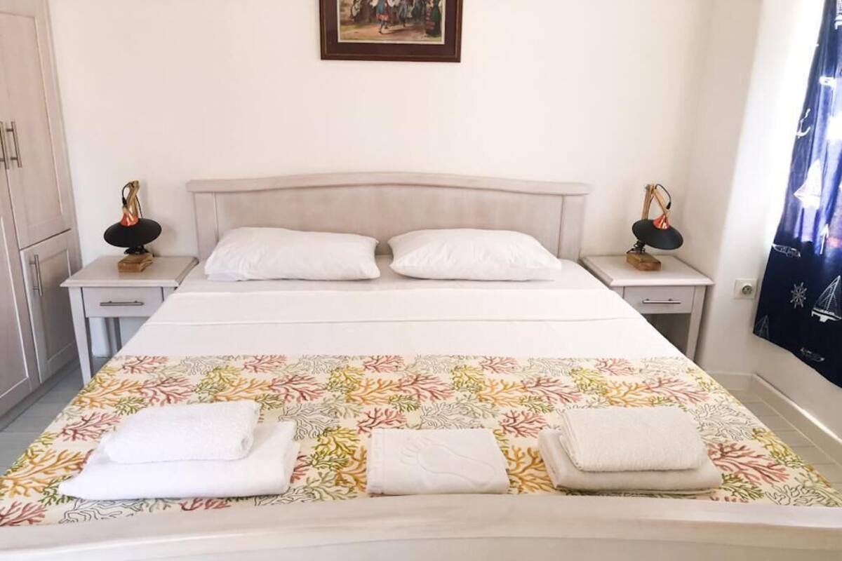 A neatly made bed with white linens and a floral-patterned bedspread. There are two bedside tables with lamps and a framed picture above the bed.