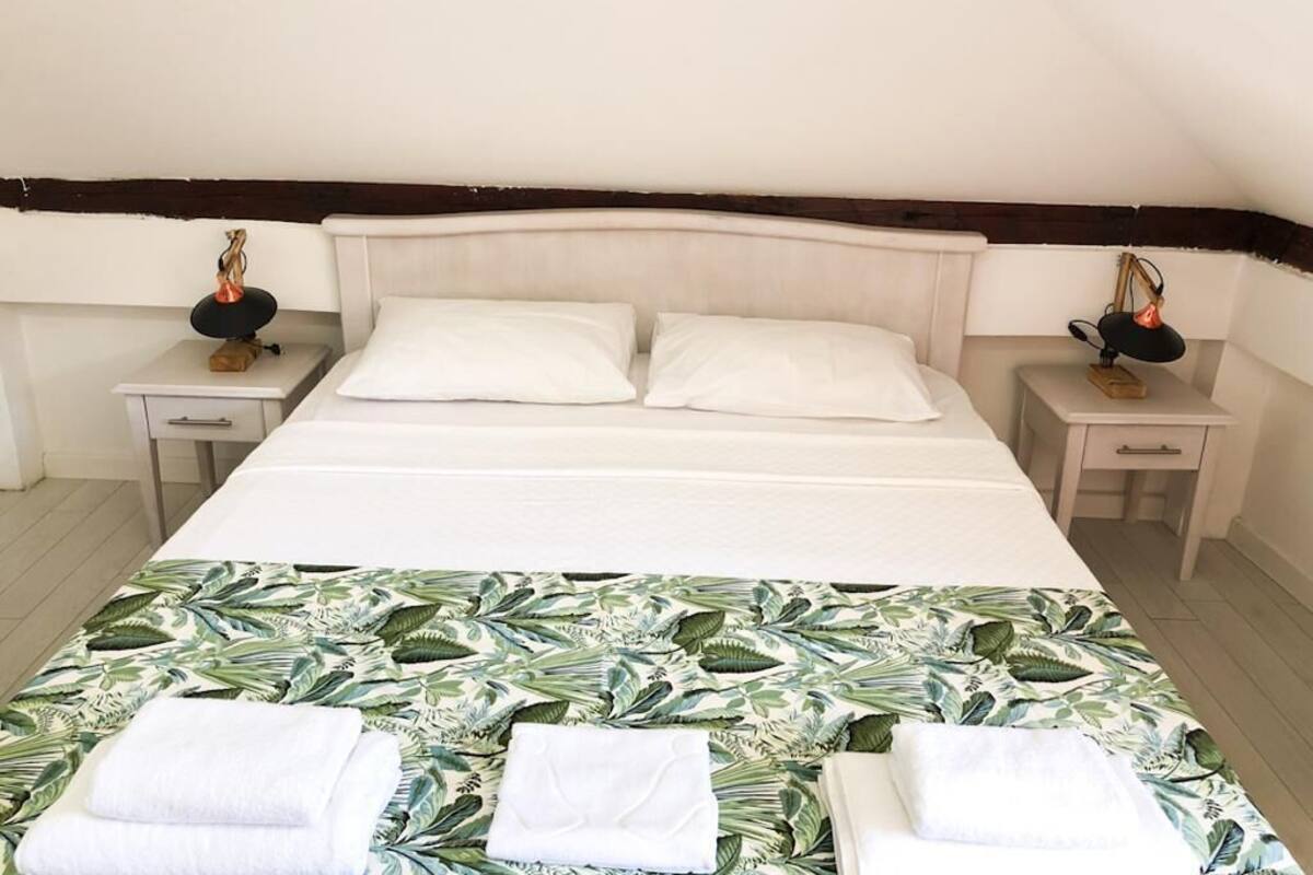 A single bed with white linens, two bedside tables with lamps, and a tropical leaf-patterned bedspread.