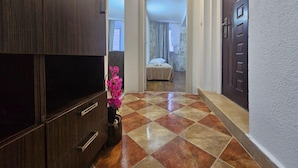A hallway with a wooden cabinet, a vase with pink flowers, and a bed in the background. - Athos Guesthouse (Kotor)