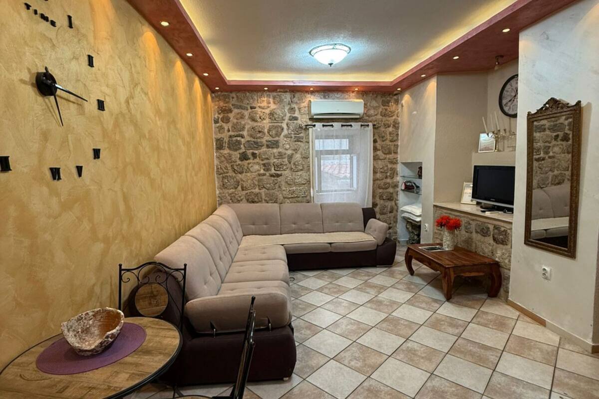 A living room with a stone wall, a sectional sofa, a round table with chairs, a TV, and a fireplace.
