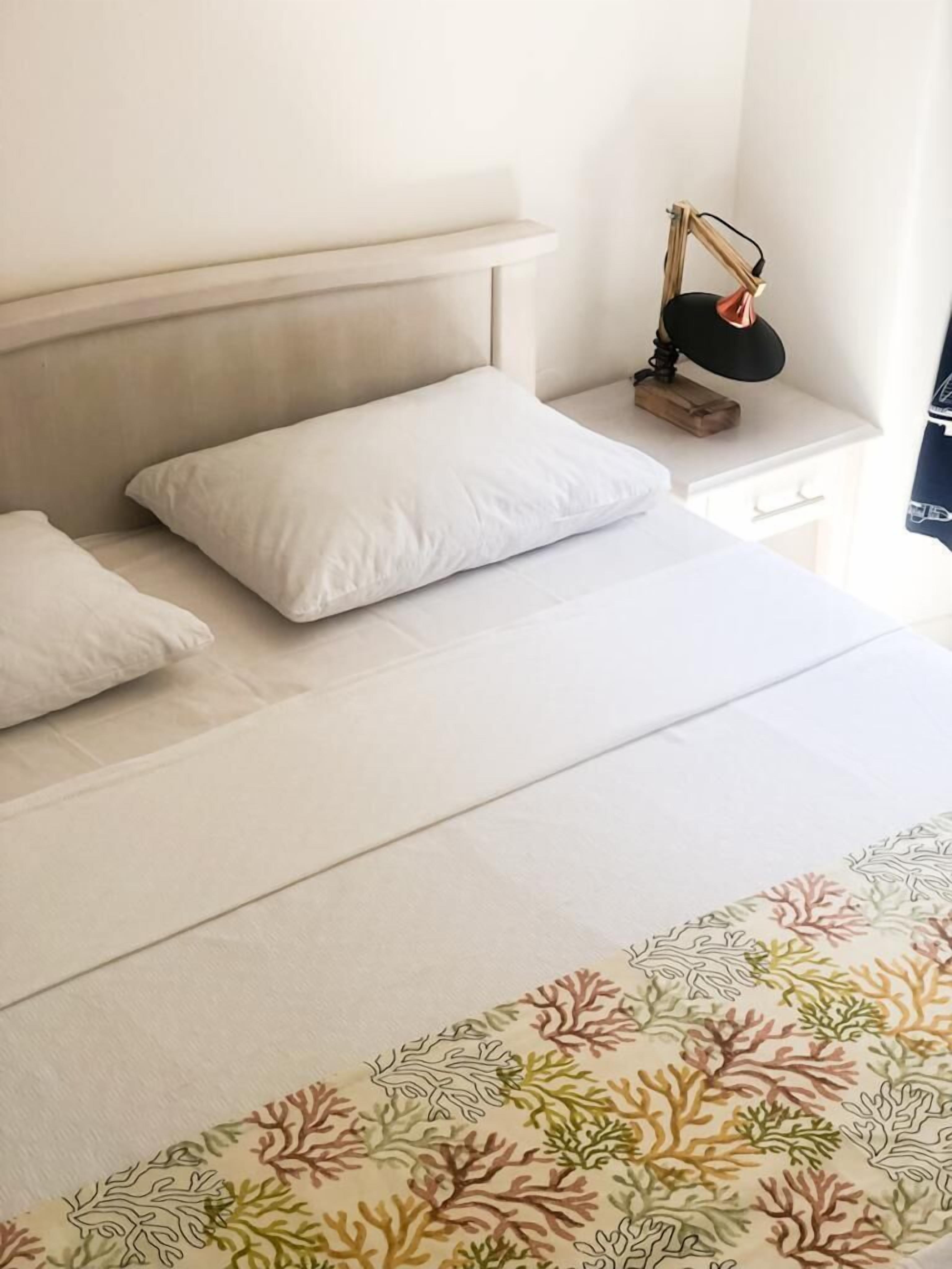 Una cama bien tendida con ropa de cama blanca y una colcha estampada en tonos coral.