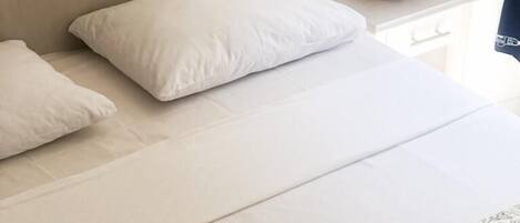 Una cama bien tendida con ropa de cama blanca y una colcha estampada en tonos coral.