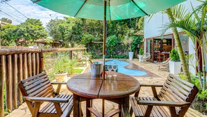 A wooden deck with a table and chairs, a green umbrella, and a pool. -  Pousada Vila Galea (Itacaré)