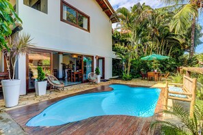 A modern house with a swimming pool, wooden deck, and tropical plants. - Pousada Vila Galea (Itacaré)