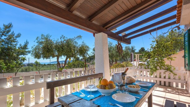 Una mesa de madera preparada para una comida, con vista al mar y a los árboles.