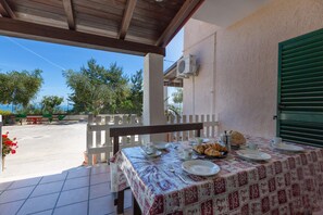Un patio techado con una mesa lista para el desayuno, asientos exteriores y vistas a árboles y una valla.