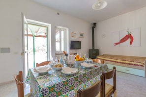 Uma sala de jantar com uma mesa posta para quatro pessoas, um sofá, uma televisão e uma janela com vista.