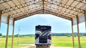 A covered parking area with a bus parked inside, a sign for Ohio State's ski and gray session, and a view of a green field. - Reconnect with nature at this unforgettable escape (RV NOT INCL'D). (Clifton)