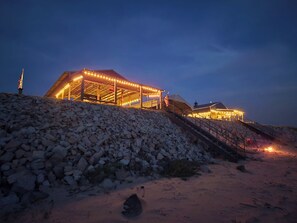 Un edificio con un espacio exterior cubierto, escaleras que lo llevan y un montón de rocas al frente.