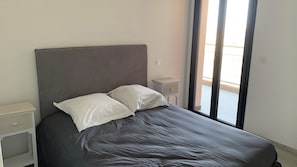 A bedroom with a bed, two pillows, a nightstand, and a window with curtains.