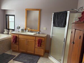A bathroom with a wooden vanity, a large mirror, a sink, a shower, and a tiled floor. - Upper Iowa River Valley Overlook, Peaceful Country Escape (Decorah)
