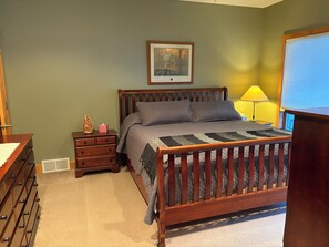 A bedroom with a wooden bed, a nightstand with a lamp, a dresser, and a framed picture on the wall. - Upper Iowa River Valley Overlook, Peaceful Country Escape (Decorah)