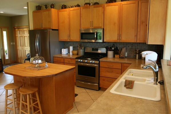 A kitchen with wooden cabinets, stainless steel appliances, a sink, and a bar area with stools. - Upper Iowa River Valley Overlook, Peaceful Country Escape (Decorah)
