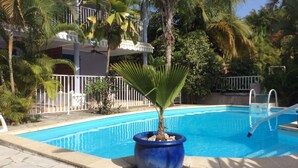 Una piscina con un macetero de palmera, una valla blanca y un edificio con balcones al fondo.
