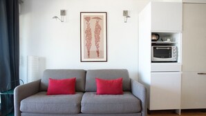 A grey sofa with red cushions, a framed artwork above it, and a white cabinet with a microwave. - *STUDIO BASIN VIEW*DIRECT ACCESS TO THE BEACH* (Arcachon)